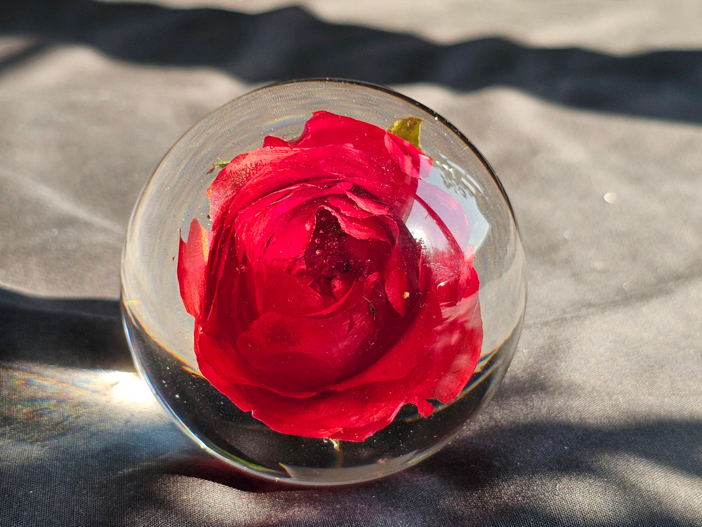 A resin sphere with a single red flower embedded in it, placed on a grey surface with a blurred background.