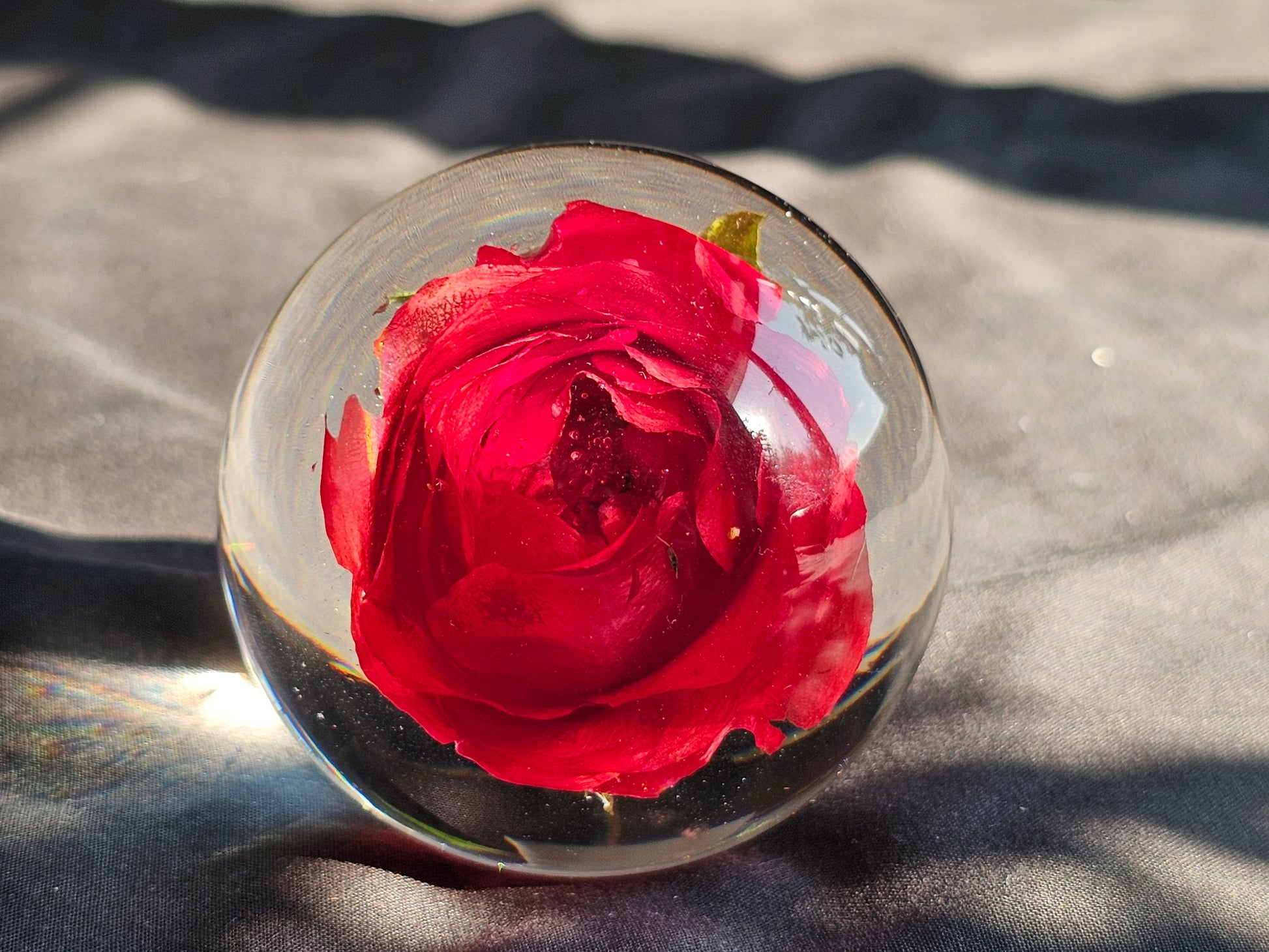 A resin sphere with a single red flower embedded in it, placed on a grey surface with a blurred background.