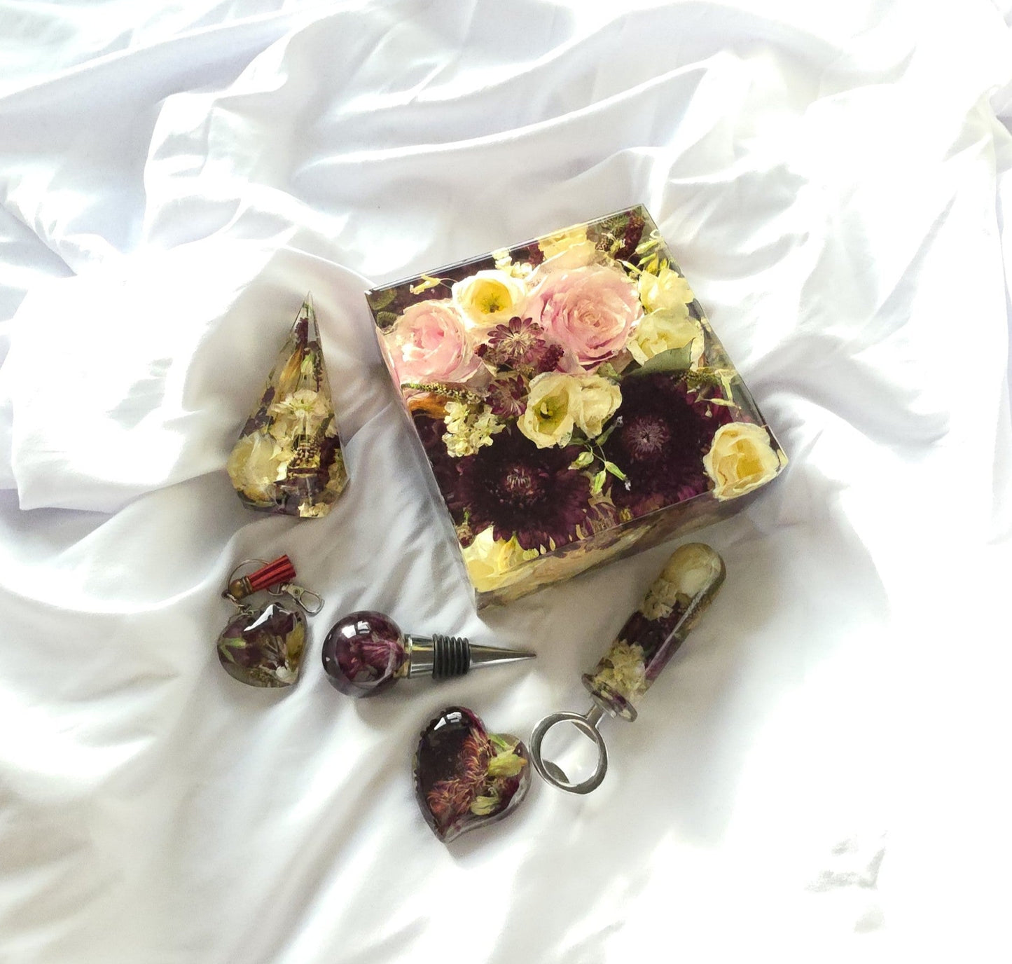 A coordinated set of resin flower keepsakes, including a square preservation block and smaller resin pieces, all made from preserved wedding flowers and arranged on white fabric.